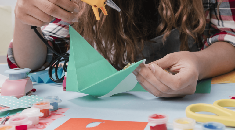 A person making paper boats with glue and scissors.