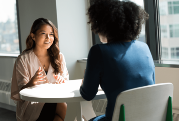 Two women sitting at a table talking to each other.