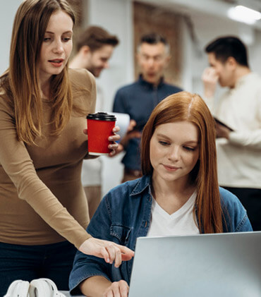 A woman is using her laptop while another person watches.