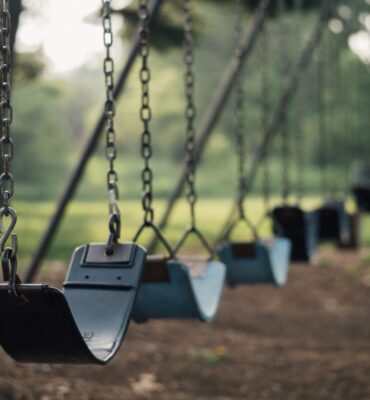 A row of swings in the park with trees in the background.