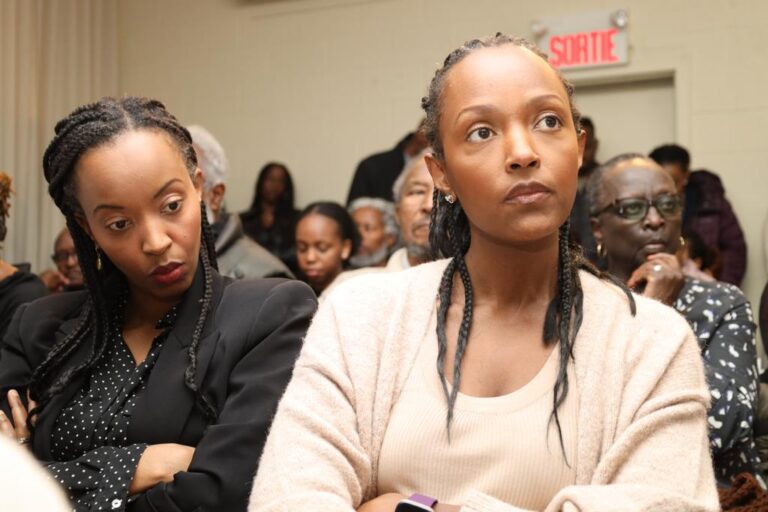Two women sitting in a room with other people.