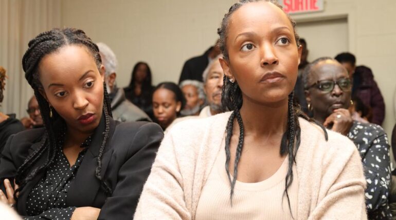 Two women sitting in a room with other people.