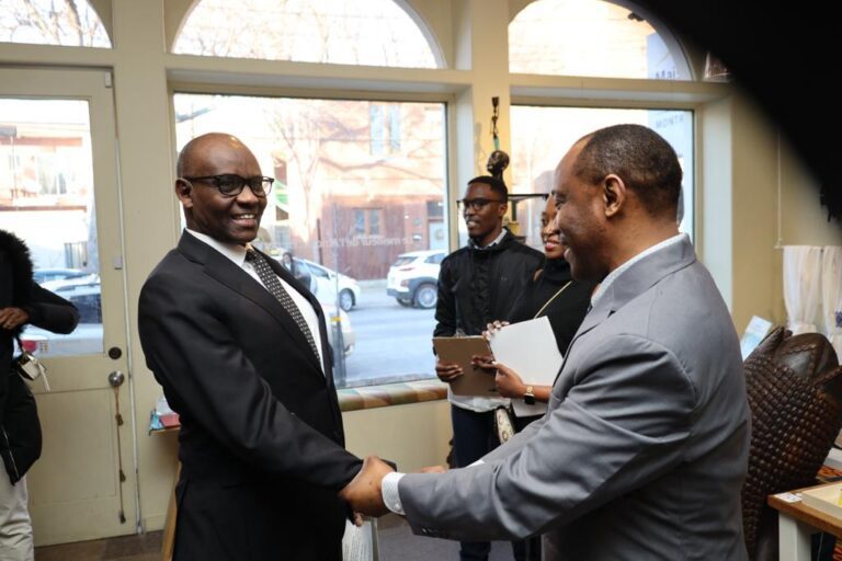Two men shaking hands in a room with other people.