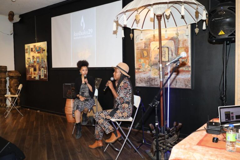 Two people sitting on chairs in front of a projector screen.