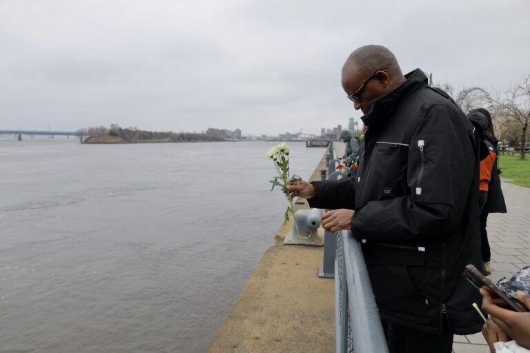 Man holding flowers by a riverside railing.