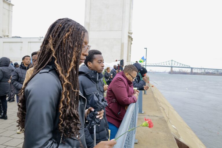 People holding flowers, standing by the river.
