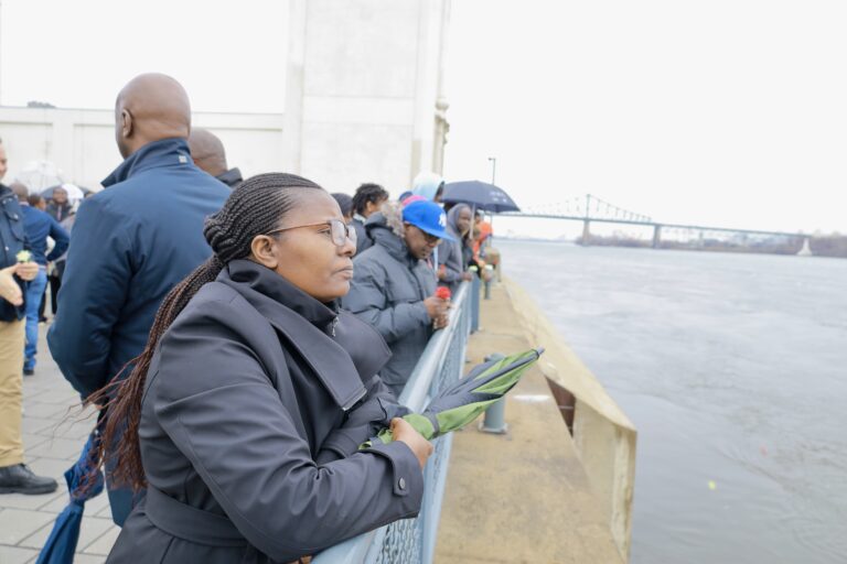 People gathered by a river holding flowers.