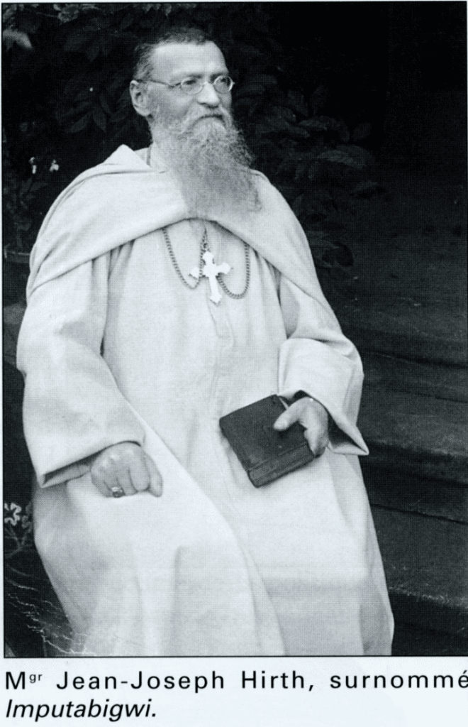 Man in robe holding a book, seated.